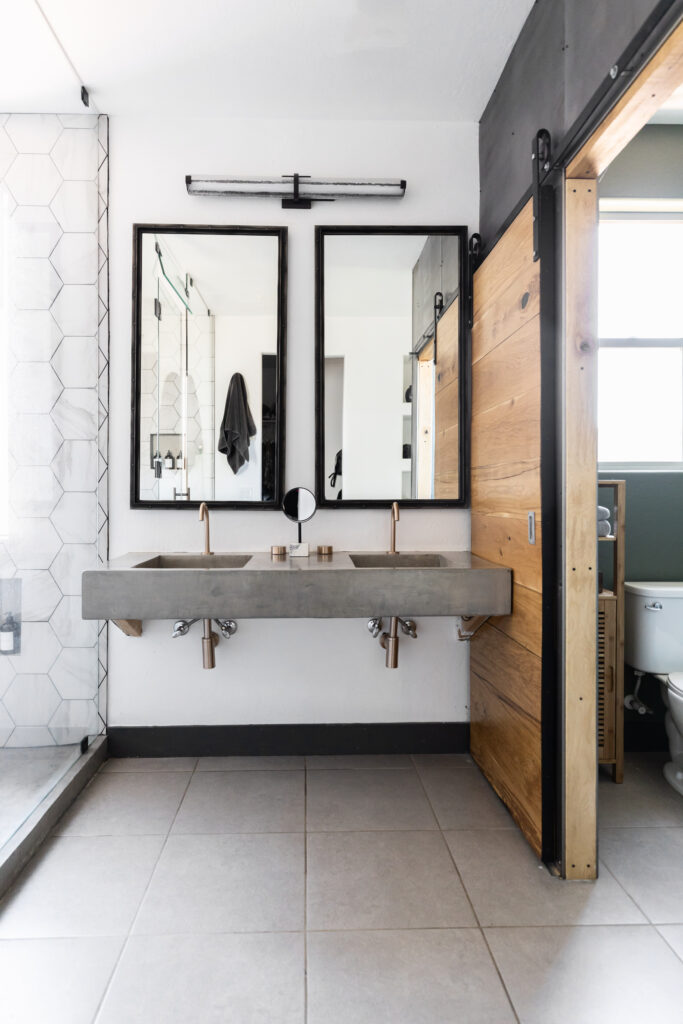 Accessible roll-under kitchen sink with open base for wheelchair users, featuring a concrete countertop, gold plumbing, and 2 mirrors